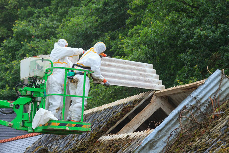 Twee mensen met beschermingspakken verwijderen golfplaten met asbest van een dak