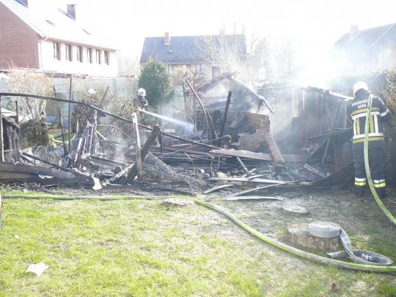 Brandweer aan het nablussen van een afgebrand gebouw in een achtertuin